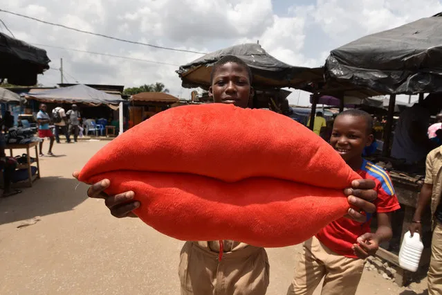 A boy poses with a pillow shaped like lips on sale for Valentine' s Day in Yopougon, a suburb of Abidjan, on February 13, 2018. (Photo by Sia Kambou/AFP Photo)