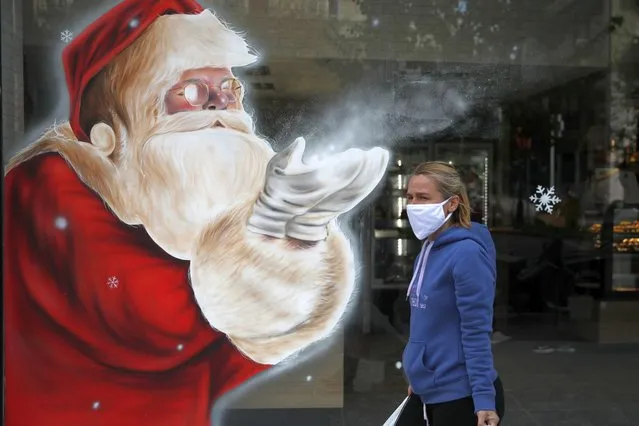 A woman wearing a face mask against the spread of coronavirus, passes a Santa Claus mural by artist Solonas which decorated the store window of a bakery in Athens, Tuesday, November 24, 2020. Greece is set to extend its lockdown measures beyond the end of November given the spread of COVID-19 and the pressure on hospitals, the country's health minister warned Monday. (Photo by Thanassis Stavrakis/AP Photo)