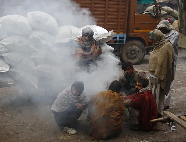 Workers warm themselves around a fire at a wholesale grocery market on a winter morning in the old quarters of Delhi December 19, 2014. (Photo by Ahmad Masood/Reuters)
