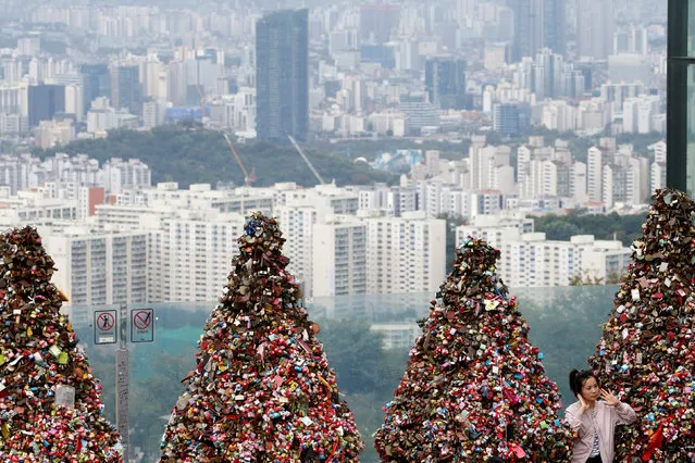 A tourist poses for photographs in front of trees covered with “love locks” as an apartment complex is seen in the background in Seoul, South Korea, August 30, 2016. (Photo by Kim Hong-Ji/Reuters)