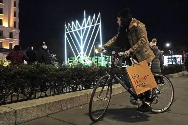 A man on a bicycle pauses on the sidewalk along Fifth Avenue in Manhattan near what has been described as “the world's largest Hanukkah menorah”, Thursday, December 10, 2020, in New York, on the first night of Hanukkah, the annual eight-day Jewish festival of lights. Due to coronavirus restrictions, a limited and socially-distanced crowd was allowed to attend. (Photo by Kathy Willens/AP Photo)