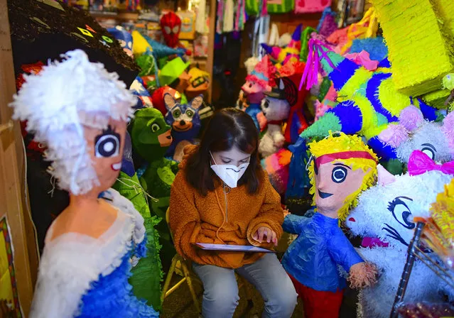 Sarita Reyes works on her school assignments on an iPad at her mother's shop, Pinata Time, on Tuesday, December 15, 2020, in San Antonio, Texas. With Fiesta canceled, children’s birthday parties called off and government officials pleading with residents to stay home during normally festive holidays, the pandemic presented a noxious brew for “piñateros” in town. (Photo by Billy Calzada/The San Antonio Express-News via AP Photo)