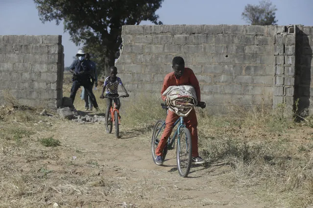 Children ride on bicycles past a wall broken by rebels from Boko Haram who kidnapped Government Science Secondary School students in Kankara, Nigeria, Tuesday, December 15, 2020. Rebels from the Boko Haram extremist group claimed responsibility Tuesday for abducting hundreds of boys from a school in Nigeria's northern Katsina State last week in one of the largest such attacks in years, raising fears of a growing wave of violence in the region. (Photo by Sunday Alamba/AP Photo)