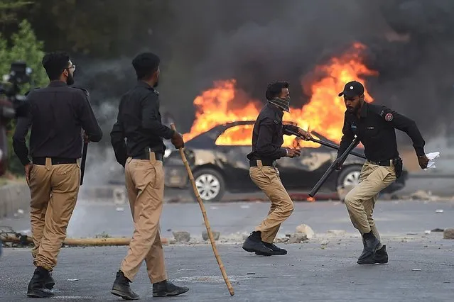 Policemen retreat after firing teargas shells towards Pakistan Tehreek-e-Insaf (PTI) party activists and supporters of former Pakistan's Prime Minister Imran near burning car during a protest against the arrest of their leader in Karachi on May 9, 2023. Former Pakistan prime minister Imran Khan was arrested on May 9, police said, during a court appearance for one of dozens of cases pending since he was booted from office last year. (Photo by Asif Hassan/AFP Photo)
