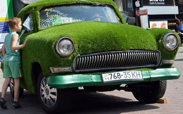 A boy looks at a GAZ-21 Volga car decorated with grass and parked in the center of Ukrainian capital of Kiev on June 13, 2013. On the windscreen, the inscriptions reads : “Make our loved Kiev green city”. (Photo by Sergei Supinsky/AFP Photo)