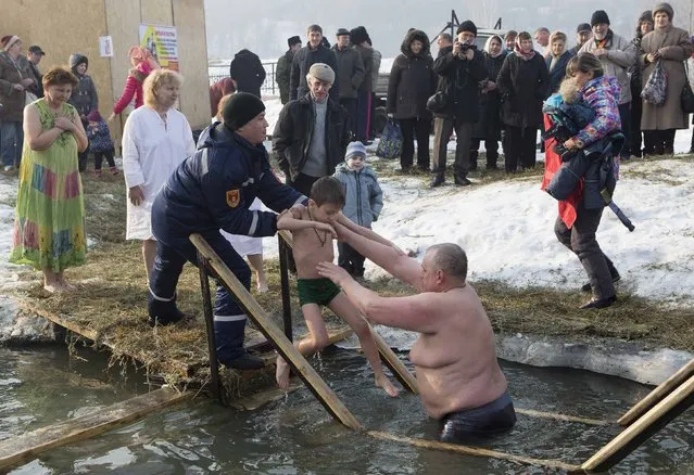 A man hands over a boy to an emergency rescuer after bathing him in the icy water of the Bolshaya Almatinka river during an Epiphany celebrations in Almaty January 19, 2015. (Photo by Shamil Zhumatov/Reuters)