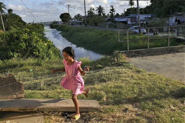 A girl runs next to a gate on the seawall in Tuschen, Guyana, Thursday, April 13, 2023. During the mid-1990s, the Inter-American Development Bank was advising Guyana to relocate communities inland since most of its people live along the coast, and much of its economic activity and agriculture are based there. But people have been reluctant to leave. (Photo by Matias Delacroix/AP Photo)