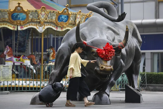 A woman pulls a 2 wheel trolley loaded with goods touches a bull statue on display outside a retail and wholesale clothing mall in Beijing, Monday, July 9, 2018. The trade war that erupted last Friday between the U.S. and China carries a major risk of escalation that could weaken investment, depress spending, unsettle financial markets and slow the global economy. (Photo by Andy Wong/AP Photo)