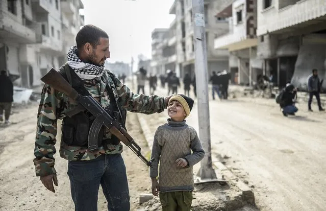 A Kurdish fighter walks with his child in the center of the Syrian border town of Kobane, known as Ain al-Arab, on January 28, 2015. (Photo by Bulent Kilic/AFP Photo)