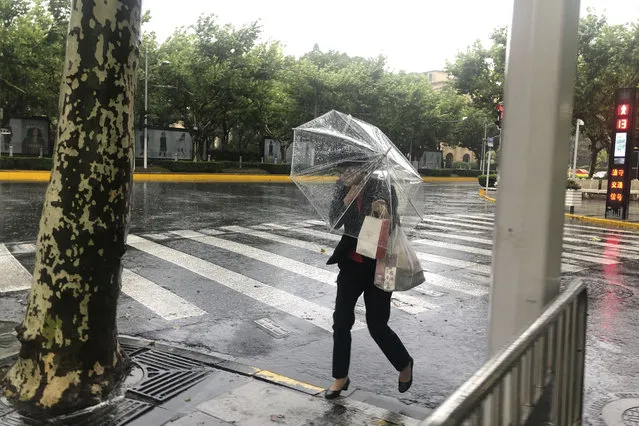 A woman carrying an umbrella braces against the wind and rain as Typhoon In-fa sweeps through Shanghai in China Sunday, July 25, 2021. (Photo by Chen Si/AP Photo)
