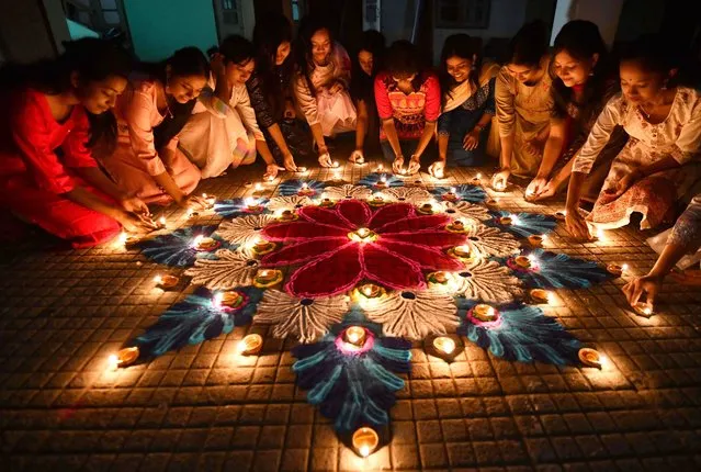 Students light earthen oil lamps on rangoli, a decorative design, on the occasion of the Diwali, a Hindu festival of lights in Guwahati on November 12, 2023. (Photo by Biju Boro/AFP Photo)