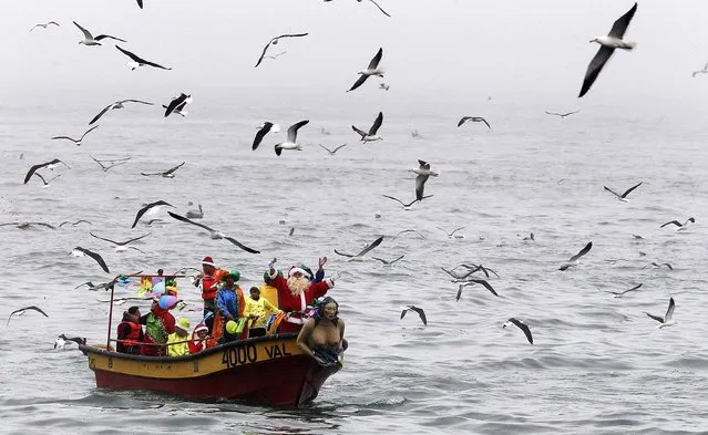 Ruben Torres, dressed in a Santa Claus outfit, wave to people from a boat along the coast of Valparaiso city, about 75 miles northwest of Santiago, Chile, on December 24, 2013. Every year, fishermen in Valparaiso organize a Santa Claus boat trip as people wait on the shore to receive their Christmas presents and well-wishes. (Photo by Eliseo Fernandez/Reuters)