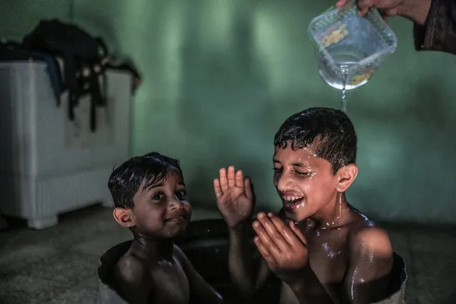 A Palestinian mother washes her sons in their house during hot weather in a slum on the outskirts of Khan Younis refugee camp, G​aza Strip, 04 August 2021. (Photo by Mohammed Saber/EPA/EFE)