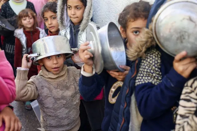 Palestinian children carry pots as they queue to receive food cooked by a charity kitchen, amid shortages in food supplies, as the conflict between Israel and Hamas continues, in Rafah in the southern Gaza Strip on December 14, 2023. (Photo by Saleh Salem/Reuters)