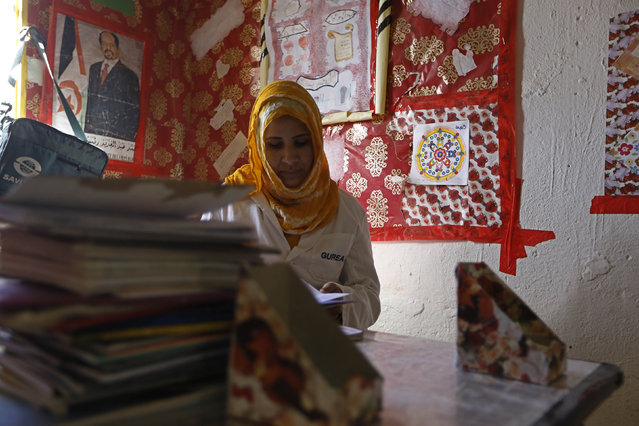 An indigenous Sahrawi teacher checks her schoolchildren's workbooks as she sits at her desk next to a photograph of Mohamed Abdelaziz, president of the Sahrawi Arab Democratic Republic, at a school in a refugee camp of Boudjdour in Tindouf, southern Algeria March 3, 2016. (Photo by Zohra Bensemra/Reuters)