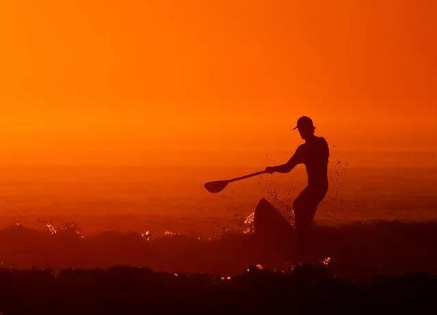 A man on a paddle board surfs during sunset at La Torche, as a heat wave hits France, in Plomeur, Brittany, France, September 6, 2021. (Photo by Pascal Rossignol/Reuters)