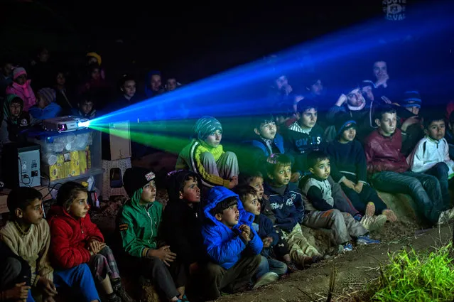 Refugees and their children sit in a field and watch cartoons projected on a side of a van near the Greek-Macedonian border near Idomeni, Greece, 05 March 2016. More than 10,000 refugees have been waiting for days to enter Macedonia. Migration restrictions along the so-called Balkan route, the main corridor for refugees and migrants heading further north to EU countries, have led to bottlenecks at the border between Greece and neighbouring Macedonia. (Photo by Georgi Licovski/EPA)