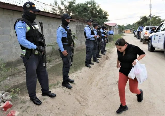 A woman walks past a line of police officers in the La Planeta neighborhood of San Pedro Sula, Honduras, Tuesday, December 6, 2022. Honduras has become the second country in Central America to impose a state of exception suspending some constitutional rights to deal with street gangs. (Photo by Delmer Martinez/AP Photo)