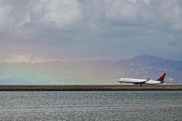A plane lands on a runway at San Francisco International Airport at the base of a rainbow on Wednesday, February 21, 2024, in San Francisco, Calif. (Photo by Lea Suzuki/San Francisco Chronicle via AP Photo)