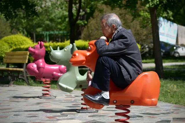 An elderly man sits on a hobby horse at a residential area in Beijing on May 4, 2015. (Photo by Wang Zhao/AFP Photo)