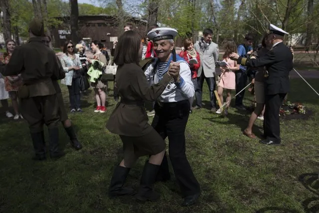 Victor Novopashin, 83, a Russian WWII veteran, center, dances with a young woman dressed in Soviet era uniform in Gorky Park in Moscow, Russia, on Saturday, May, 9, 2015, during the commemorations for the 70th anniversary of victory over Nazi Germany. (Photo by Alexander Zemlianichenko Jr./AP Photo)