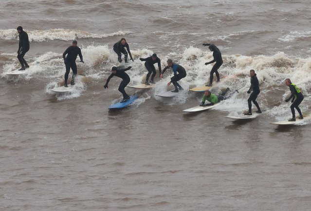 Surfers ride the Severn Bore surge wave, a natural phenomenon occurring according to the lunar cycle where a set of waves push through the Severn River estuary and upstream on a high tide, on the only day in 2024 where it is given a five-star size status, at Newnham, near Gloucester in Britain, on March 12, 2024. (Photo by Toby Melville/Reuters)