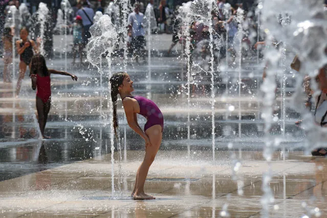 Children cool off in the water fountains in Nice, southeastern France, Sunday, July 5, 2015. A mass of hot air moving north from Africa is bringing unusually hot weather to Western Europe, with France in recent days experiencing temperatures around 34 degrees Celsius (93 Fahrenheit). (Photo by Lionel Cironneau/AP Photo)
