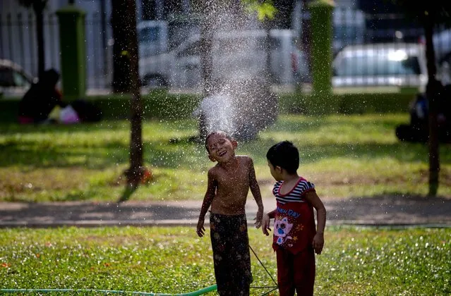 Children play with a garden water spurt in a hot and humid day at a public park in Yangon, Myanmar, Tuesday, April 22, 2014. In Yangon during the month of April, temperature rises up to 37 degrees Celsius (98 degrees Fahrenheit) with up to 94 percent humidity before the tropical rainy season starts in May. (Photo by Gemunu Amarasinghe/AP Photo)