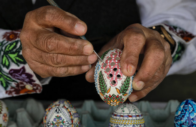 In this Thursday, April 13, 2017, picture artisan Nicu Poenariu demonstrates his technique on an Easter egg on sale at a fair in Bucharest, Romania. (Photo by Vadim Ghirda/AP Photo)