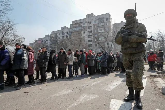 A Russian army soldier stands next to local residents who queue for humanitarian aid delivered during Ukraine-Russia conflict, in the besieged southern port of Mariupol, Ukraine on March 23, 2022. (Photo by Alexander Ermochenko/Reuters)