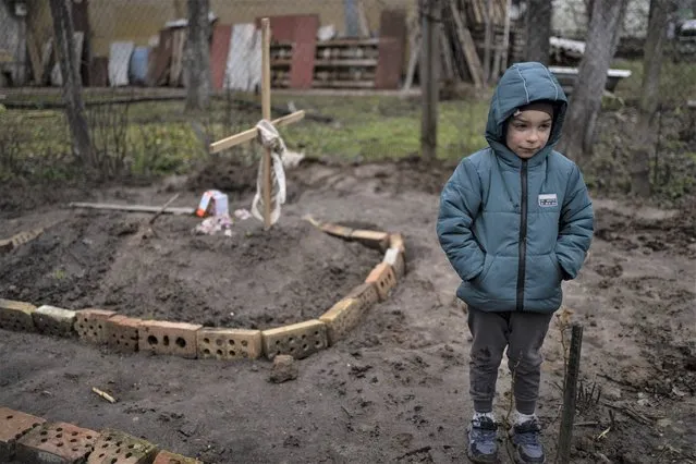 In the courtyard of their house, Vlad Tanyuk, 6, stands near the grave of his mother Ira Tanyuk, who died because of starvation and stress due to the war, on the outskirts of Kyiv, Ukraine, Monday, April 4, 2022. (Photo by Rodrigo Abd/AP Photo)