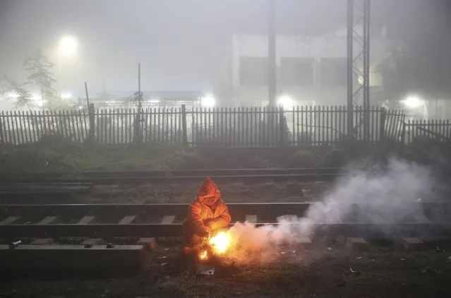 A Railway railway employee warms himself in front of a bonfire surrounded by fog early morning in Prayagraj, India, Saturday, January 18, 2020. Large parts of north India experience weeks of thick fog in the winter season, that disrupts rail and air traffic as well as normal life. (Photo by Rajesh Kumar Singh/AP Photo)