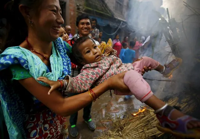 A woman swings a child around a fire, where an effigy of the demon Ghantakarna was burnt to symbolize the destruction of evil, during the Ghantakarna festival at the ancient city of Bhaktapur, Nepal August 12, 2015. (Photo by Navesh Chitrakar/Reuters)