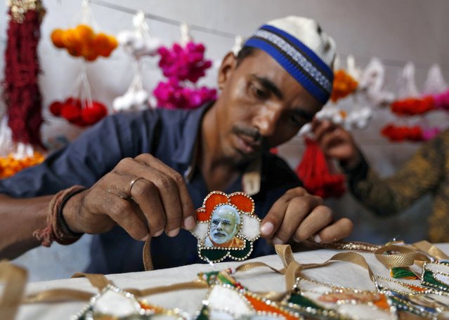 A Muslim artisan displays a “rakhi” or traditional Indian sacred thread, featuring India's Prime Minister Narendra Modi after giving it the finishing touches inside a workshop in Ahmedabad August 17, 2015. Rakhi is also the name of a Hindu festival, also known as Raksha Bandhan, during which a sister ties one or more of the sacred threads onto her brother's wrist to ask him for her protection. The festival will be celebrated across the country on August 29 this year. (Photo by Amit Dave/Reuters)
