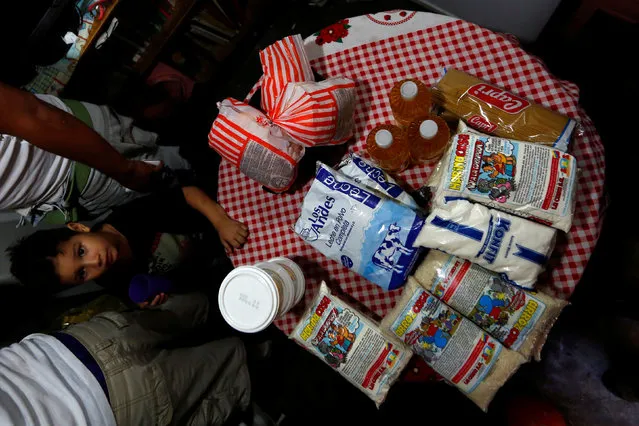 Families display the food staples which they bought under a new government system in providing basic food at low cost, in Caracas, Venezuela July 9, 2016. (Photo by Carlos Jasso/Reuters)