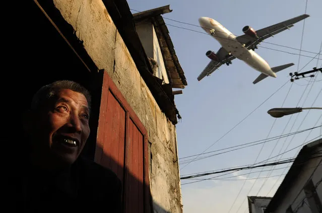 A man watches as an airliner flies over his house into Hongqiao International airport in Shanghai on January 5, 2012. (Photo by Peter Parks/AFP Photo)