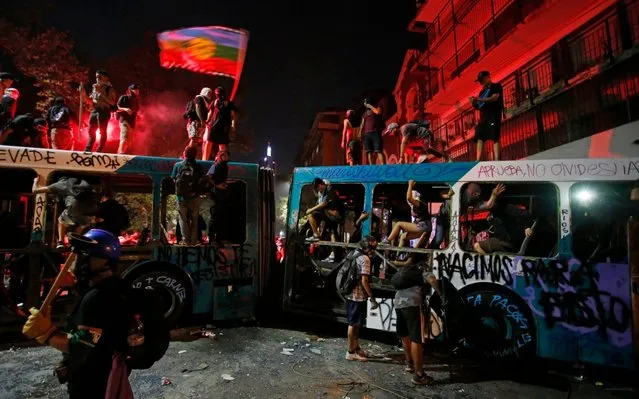 Demonstrators stand on a destroyed a bus during an anti-government protest in Santiago, Chile, Friday, March 13, 2020. Chile has been roiled by continuing street protests since Oct. 18 of last year, when a student protest over a modest increase in subway fares turned into a much larger and broader movement with a long list of demands that largely focus on inequality. (Photo by Luis Hidalgo/AP Photo)