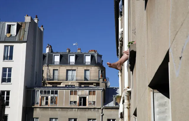 The feet of a woman dangle from a window ledge in the sun during a nationwide confinement to counter the Covid-19 virus, in Paris, Sunday, April 5, 2020. (Photo by Francois Mori/AP Photo)