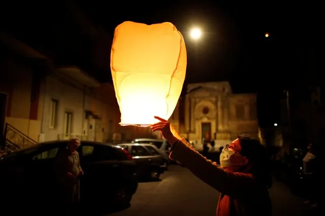 A woman wearing a protective face mask lights a paper lantern as she attends a celebration in memory of those who died due to the outbreak of the coronavirus disease (COVID-19), in the small southern town of San Giorgio Ionico, Itay on April 12, 2020. (Photo by Alessandro Garofalo/Reuters)