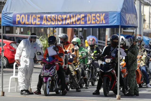 A policeman wearing a protective suit checks motorcycle riders at a checkpoint during an enhanced community quarantine to prevent the spread of the new coronavirus at the outskirts of Manila, Philippines on Monday April 27, 2020. (Photo by Aaron Favila/AP Photo)