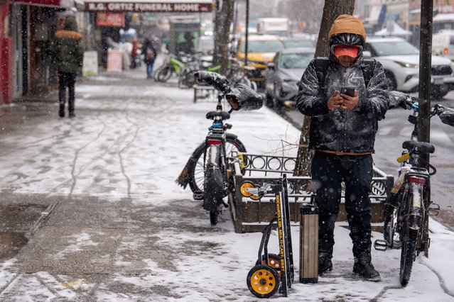 A delivery worker looks at his phone during a snowfall in the Harlem Section of New York City, on January 6, 2025. (Photo by David Dee Delgado/Reuters)