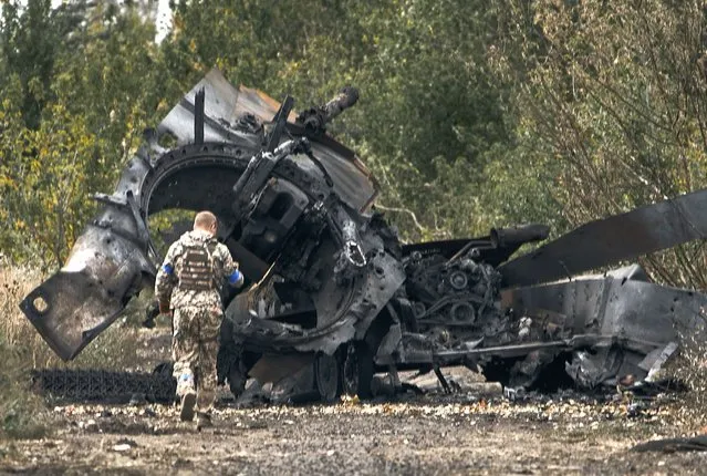 A Ukrainian soldier passes by a Russian tank damaged in a battle in a just freed territory on the road to Balakleya in the Kharkiv region, Ukraine, Sunday, September 11, 2022. (Photo by AP Photo/Stringer)