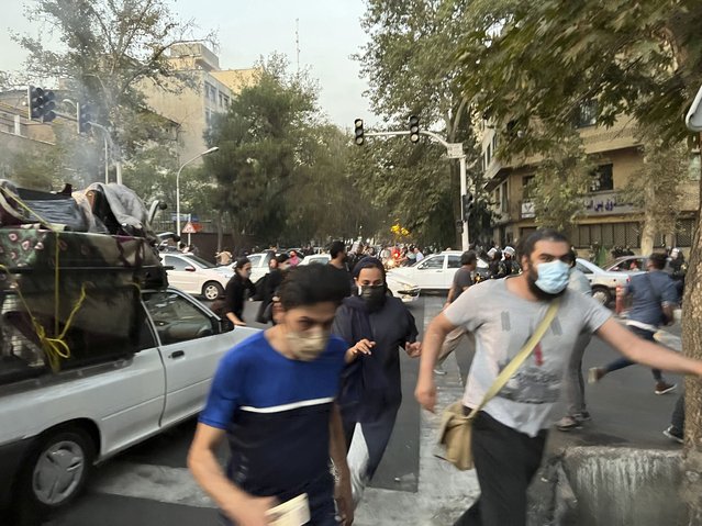 In this Monday, September 19, 2022, photo taken by an individual not employed by the Associated Press and obtained by the AP outside Iran, people run away from anti-riot police during a protest over the death of a young woman who had been detained for violating the country's conservative dress code, in downtown Tehran, Iran. (Photo by AP Photo/Stringer)