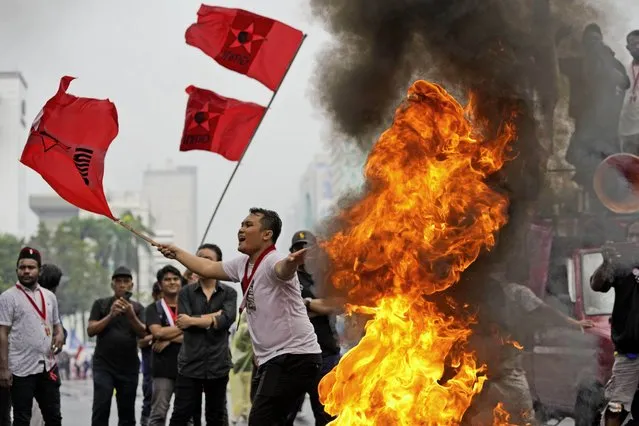 Student activists wave flags as they burn a tire during a rally against sharp increases in fuel prices, in Jakarta, Indonesia, Thursday, September 8, 2022. The Indonesian government increased the fuel prices by about 30% on Saturday after reducing some of the costly subsidies that have helped control inflation in the country. (Photo by Achmad Ibrahim/AP Photo)