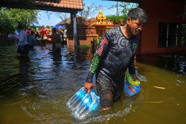 A man carries bottles of water while walking in a flooded street in Ayutthaya, Thailand on October 13, 2022. (Photo by Chalinee Thirasupa/Reuters)