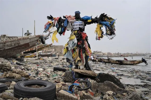 The environmental activist Modou Fall, who many simply call “Plastic Man”, poses for a photo at the Yarakh Beach littered by trash and plastics in Dakar, Senegal, Tuesday, November 8, 2022. As he walks, plastics dangle from his arms and legs, rustling in the wind while strands drag on the ground. On his chest, poking out from the plastics, is a sign in French that says, “No to plastic bags”. (Photo by Leo Correa/AP Photo)