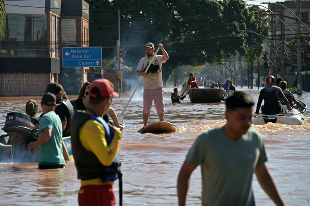 A man moves on in a SUP board following floodings due to heavy rains in Porto Alegre, Rio Grande do Sul state, Brazil on May 6, 2024. From top to bottom, rescuers scour buildings in Porto Alegre for inhabitants stuck in apartments or on rooftops as unprecedented flooding killed at least 78 people in the southern state, with dozens missing and some 115,000 forced to leave their homes. (Photo by Nelson Almeida/AFP Photo)