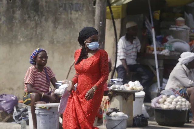 A woman wearing a face mask to protect against coronavirus, walks past people selling food at a market in Lagos, Nigeria, Thursday December 24, 2020. Africa’s top public health official says another new variant of the coronavirus appears to have emerged in Nigeria, but further investigation is needed. The discovery could add to new alarm in the pandemic after similar variants were announced in recent days in Britain and South Africa and sparked the swift return of travel restrictions. (Photo by Sunday Alamba/AP Photo)
