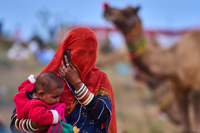 A woman holds her child as she talks on a phone at the annual cattle fair in Pushkar, in the western Indian state of Rajasthan, Sunday, October 26, 2025. (Photo by Rajesh Kumar Singh/AP Photo)
