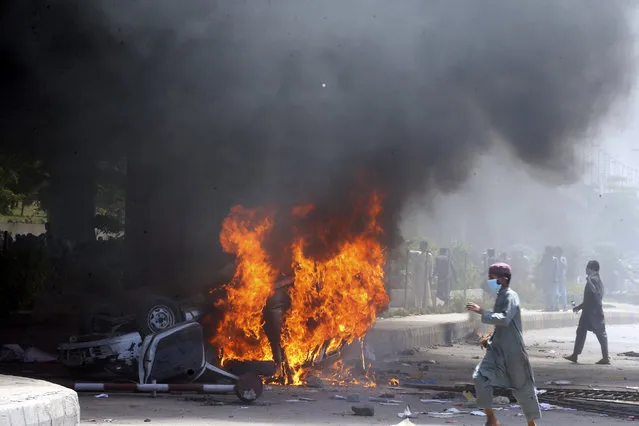 Supporters of Pakistan's former Prime Minister Imran Khan walk next to a burning car during a protest against the arrest of their leader, in Peshawar, Pakistan, Wednesday, May 10, 2023. Pakistan braced for more turmoil a day after Khan was dragged from court in Islamabad and his supporters clashed with police across the country. The 71-year-old opposition leader is expected in court later Wednesday for a hearing on keeping Khan in custody. (Photo by Muhammad Sajjad/AP Photo)